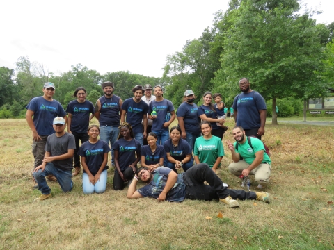 a group of people wearing purple and green shirts standing in a green field of a nature park