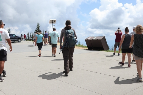 Several people on a wide sidewalk beside a parking lot