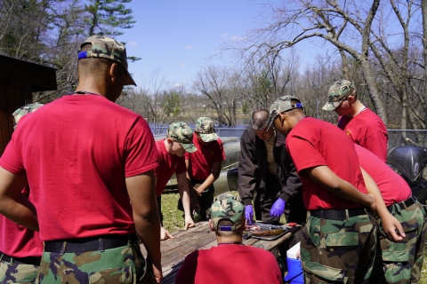 USFWS biologist teaches a group of eight students in military camo how to filet a fish