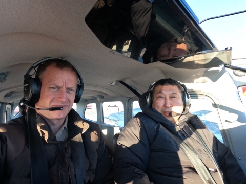 Two people sit in the cockpit of a single engine plane with headsets on. 