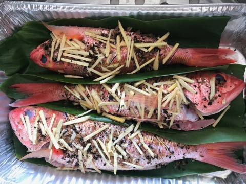 Three red fish in leaves are seasoned for cooking