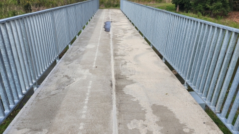 Close-up image of a cream colored concrete surface on a footbridge with gray metal railings on both sides.
