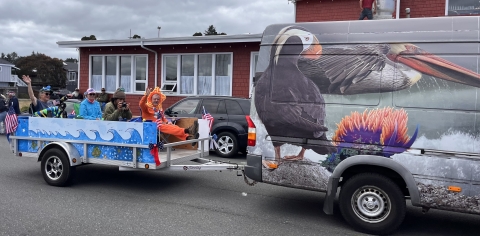 A van pulls a trailer decorated with waves as a parade float.