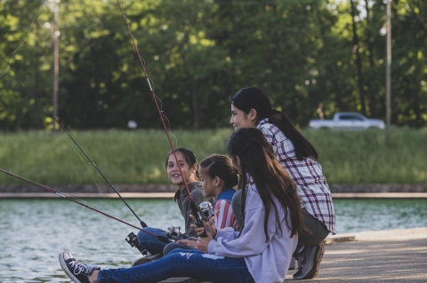 Woman and three children fishing while sitting on dock