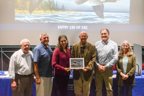 Six judges at the 2025 Federal Duck Stamp Art Contest hold the winning artwork.