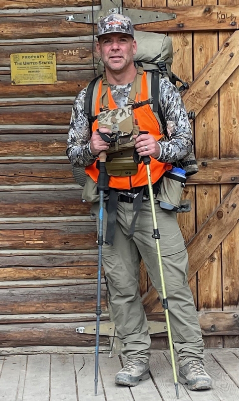 man in camo, orange vest holding hiking poles