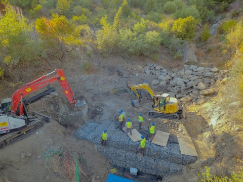 An image from above of people in high visibility vests standing on a rock wall on a mountainside