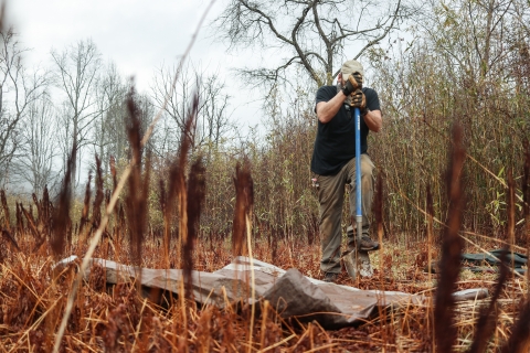 Man standing in a field, digging with a shovel