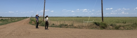 2 people seen at a dirt road crossing in the region where Texas kangaroo rat burrows are all around. One researcher seen pointing in the distance, both looking towards the pointing hand.