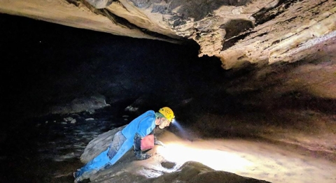 A man wearing a head lamp studies the floor of a dark cave.