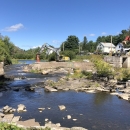 Concrete dam spans halfway across a river with heavy machinery and people in construction hats on top