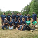 a group of people wearing purple and green shirts standing in a green field of a nature park