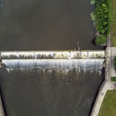 Aerial view of a dam in a dark river with green grass on both side