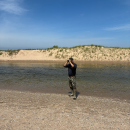 A man standing on a beach looking through binoculars away from the water.