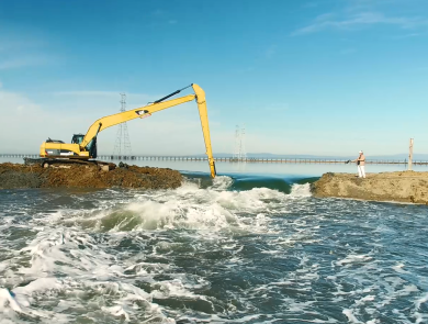 A bulldozer works to remove part of an earthen levy separating two bodies of water.