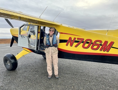 Kara Hilwig standing next to a single engine bush plane on a dirt airstrip.