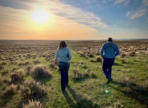 two people walking towards sunset through sagebrush landscape