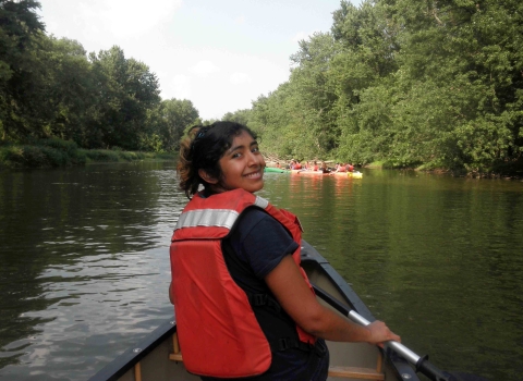A latina woman wearing an orange personal flotation device canoeing on a river