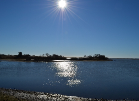 The sun in a crystal clear blue shy over a piece of land jutting into water